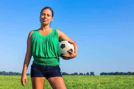 Standing young colombian woman holding football in front of blue skyの写真素材