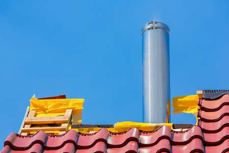 New roof with roof tiles and stainless metal chimney pipe against blue skyの写真素材