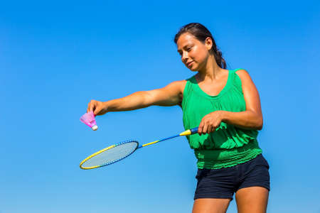Young Colombian woman serve with badminton racket and shuttle in front of blue skyの写真素材