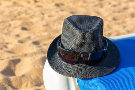 Gray sun hat and sunglasses on blue beach bed at coastの写真素材