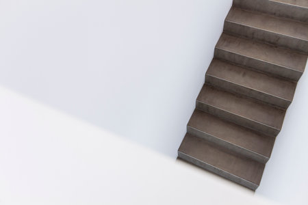 Close-up view of a minimalist concrete staircase ascending in a modern interior space. The design features clean lines and a stark contrast between the textured dark concrete and smooth white walls, creating a sleek, industrial aesthetic. Ideal for concepts related to architecture, interior design, minimalism, and modern living.の写真素材