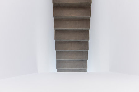 Close-up view of a minimalist concrete staircase ascending in a modern interior space. The design features clean lines and a stark contrast between the textured dark concrete and smooth white walls, creating a sleek, industrial aesthetic. Ideal for concepts related to architecture, interior design, minimalism, and modern living.の写真素材