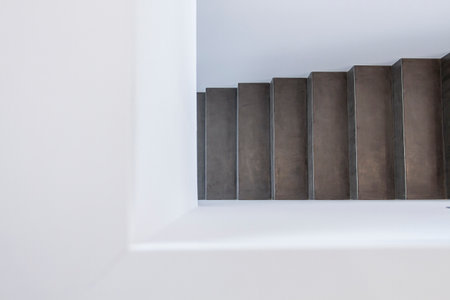 Close-up view of a minimalist concrete staircase ascending in a modern interior space. The design features clean lines and a stark contrast between the textured dark concrete and smooth white walls, creating a sleek, industrial aesthetic. Ideal for concepts related to architecture, interior design, minimalism, and modern living.の写真素材