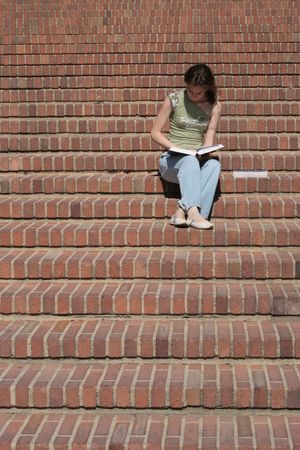 Young lady reads a book sitting on stairsの写真素材