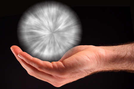A hand holding a white ball of light against a black background.の写真素材