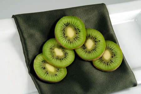 An arrangement of kiwi on a decorative green napkin on a white plate against a white background.の写真素材