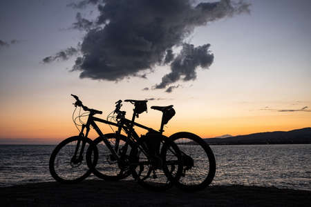 Two mountain bikes stand on the edge of a cliff, where you can see a bright orange sea sunset, mountains and large clouds. Recreation and sports in the resort city of Gelendzhikの写真素材