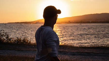Silhouette of a guy at sunset, close-up. In the bright rays of the sun, he rests in the Park and looks at the evening seascape. The city resort of Gelendzhik, the black sea coastの写真素材