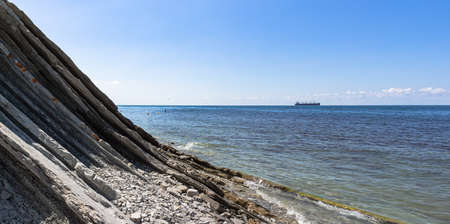 Panorama of the seascape. Picturesque stone wild beach at the foot of the cliffs, bright blue sky...