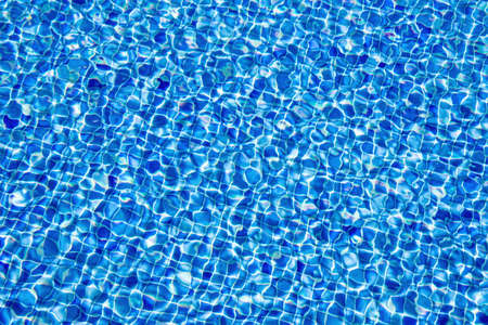 An abstract background of clear water in a dark blue tiled swimming pool 