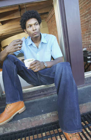 Man sitting on a window ledge eating olivesの写真素材