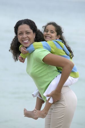 Young girl piggyback riding on a young woman at the beachの写真素材