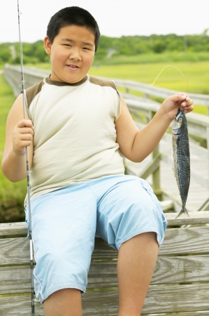 Young boy sitting holding a fishing rod and a fishの写真素材