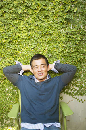 Mid adult man sitting on a chair with his hands behind his headの写真素材