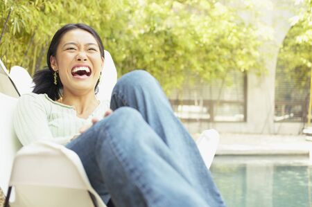 Young woman sitting on a chair outdoors laughingの写真素材
