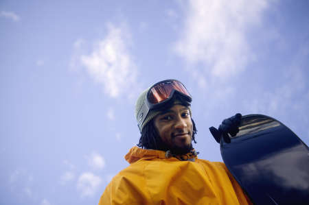 Low angle view of a young man holding a snowboardの写真素材