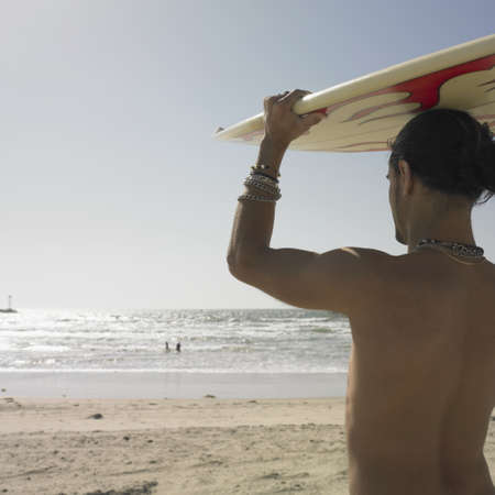 Rear view of a young man carrying surfboard on his headの写真素材