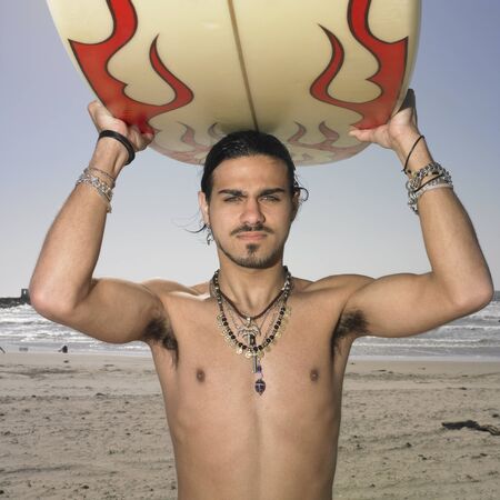 Portrait of a young man carrying a surfboard on his head