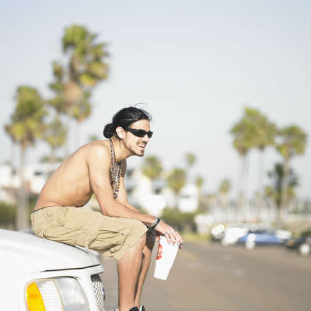 Side profile of a young man sitting on a car bumperの写真素材