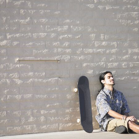 Young man sitting against a stone wall