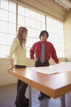 Businessman and a businesswoman discussing blueprints in an officeの写真素材