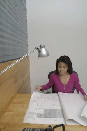 High angle view of a businesswoman listening to music and looking at blueprints in an office