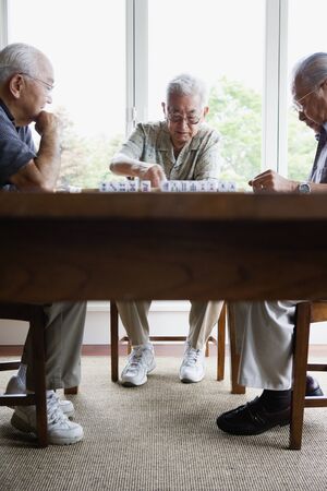 Three elderly men sitting at table playing gameの写真素材