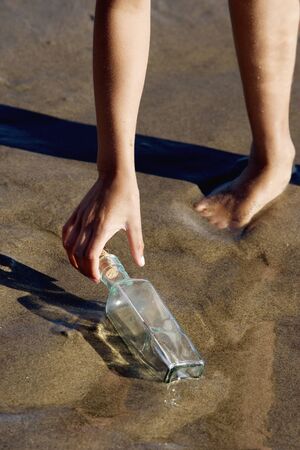 Low section of girl picking up bottle on beachの写真素材