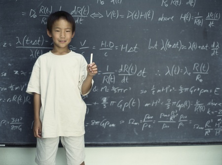 Portrait of boy holding chalk standing in front of chalkboardの写真素材