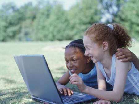 Two girls laying in park with laptopの写真素材