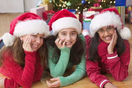 Portrait of three girls with Santa hats in front of Christmas treeの写真素材
