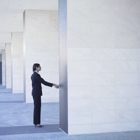 Businesswoman shaking hand behind wallの写真素材