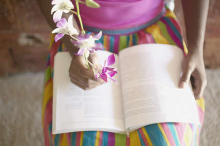 Low section of woman sitting in chair reading book while holding flowersの写真素材