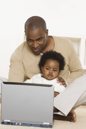 Father using laptop and holding baby daughterの写真素材