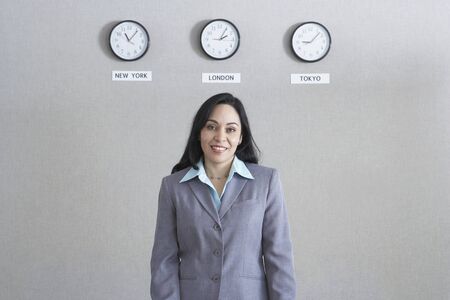 Hispanic businesswoman standing under world time zone clocks