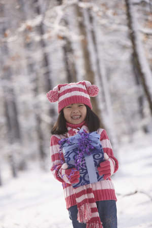 Young Asian girl holding gift in snow outdoors