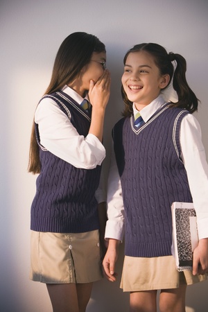 Two school girls in uniform whisperingの写真素材