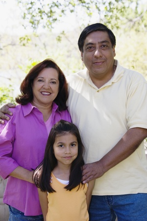 Hispanic grandparents and granddaughter hugging outdoorsの写真素材