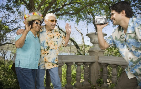 Young man using video camera to film senior couple wavingの写真素材