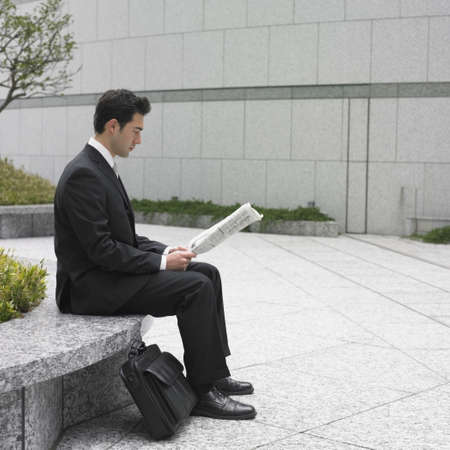 Businessman reading newspaper on bench outdoorsの写真素材
