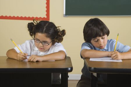 Children writing at desks in classroomの写真素材