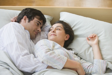 Hispanic couple smiling at each other in bedの写真素材