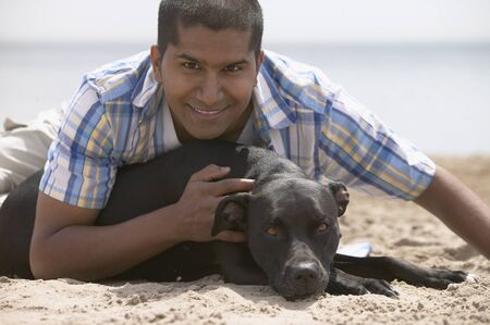 Indian man and dog sitting on beachの写真素材