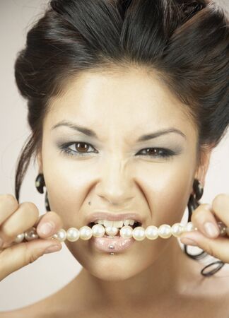 Woman with hair up biting pearl necklaceの写真素材