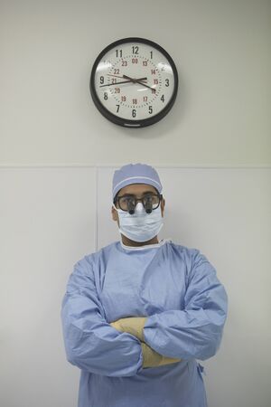 Male surgeon standing under wall clockの写真素材