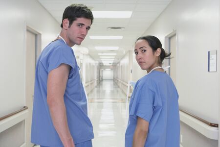 Rear view of male and Hispanic female doctors looking over shoulder in corridorの写真素材