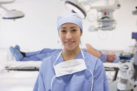 Hispanic female doctor smiling in operating room with male doctor laying on table in backgroundの写真素材