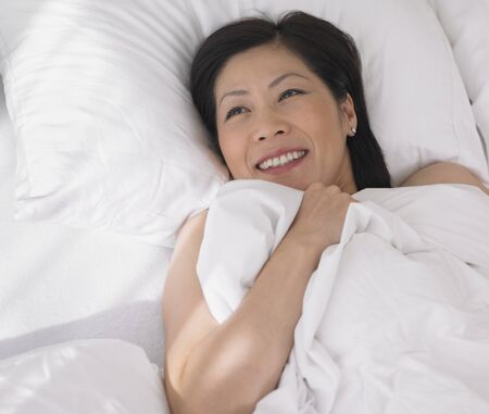Middle-aged Asian woman laying in bedの写真素材