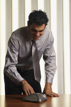 Hispanic businessman using speakerphone on conference tableの写真素材
