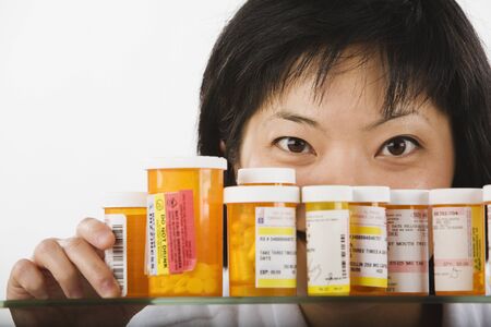Asian woman looking over bottles of medicationの写真素材